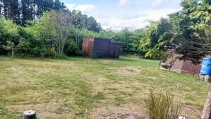 A grassy backyard with a shed, a blue barrel, and a concrete planter with plants. - 6 Person Holiday Home in Brovst (Brovst)