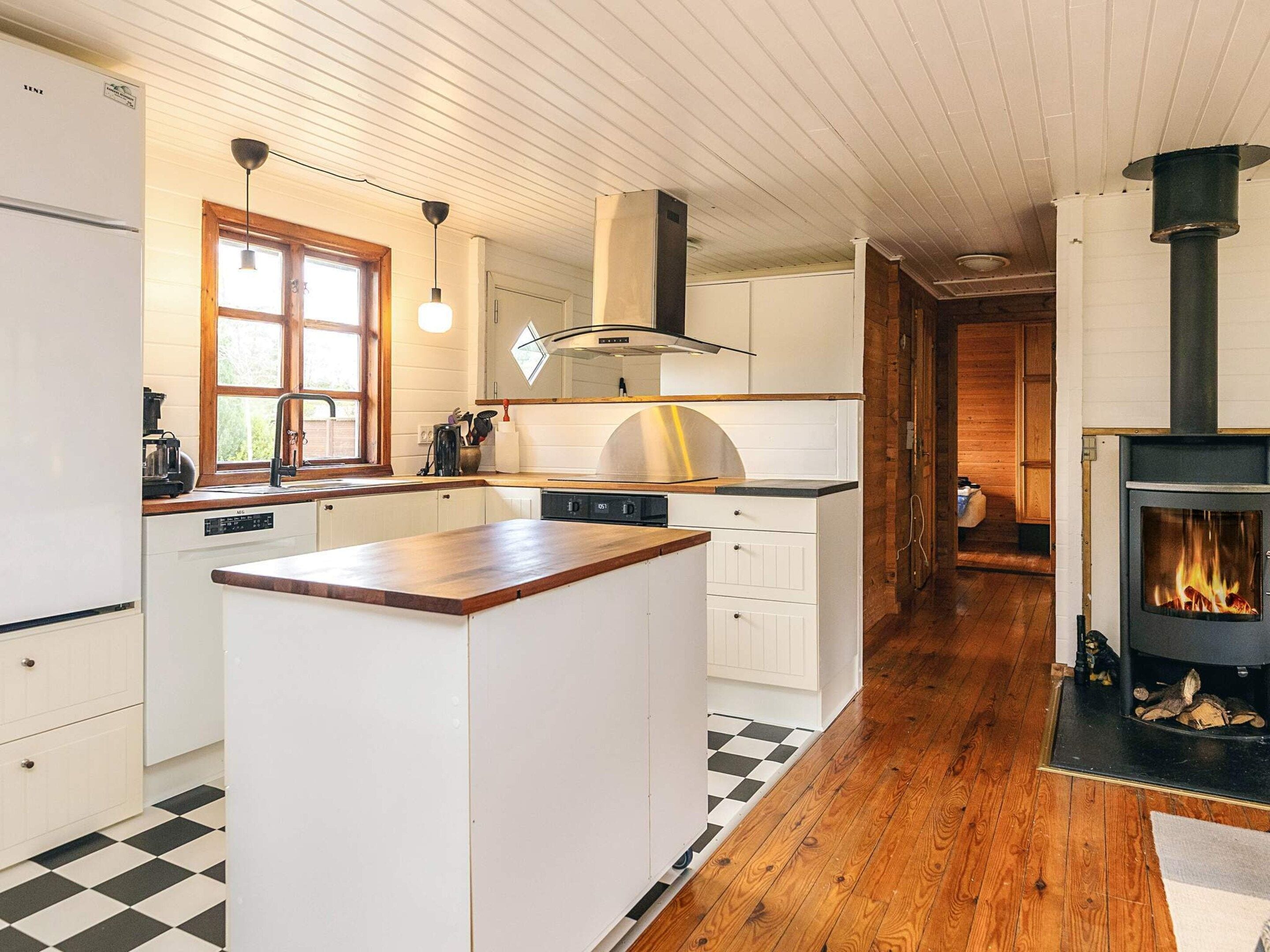 A modern kitchen with a central island, wooden flooring, and a built-in wood-burning stove.
