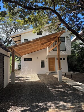 A modern two-story house with a covered patio, a gravel driveway, and a wooden door. - Quality Home in Perfect Location Close to Beach & Restaurants (Sámara)