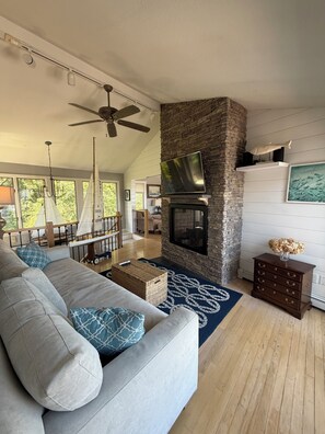 A spacious living room with a stone fireplace, a large sofa, and a television mounted on the wall. - Marvelous 5-bed house steps to Cliff House, minutes to Perkins Cove and Ogunquit (Cape Neddick)