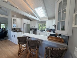 A modern kitchen with white cabinetry, a central island with bar stools, and a skylight. - Marvelous 5-bed house steps to Cliff House, minutes to Perkins Cove and Ogunquit (Cape Neddick)