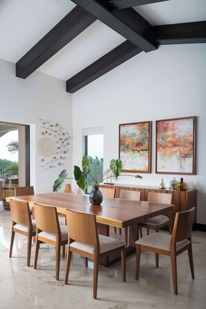 A modern dining area with a wooden table and chairs, a vase with a plant, and abstract art on the wall. - Ocean & Golf View Penthouse | Private Chef & Cart (Punta de Mita)