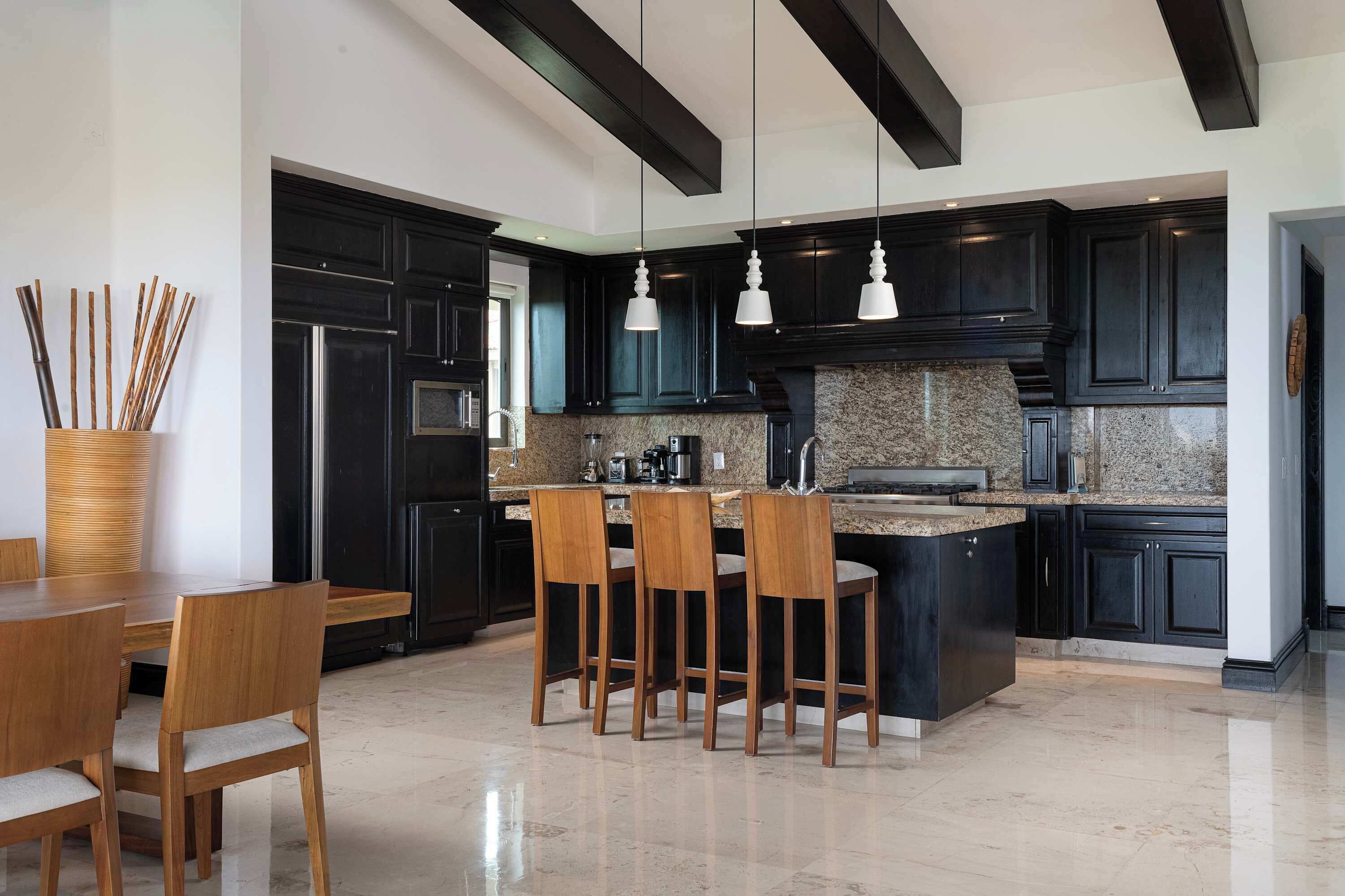 A modern kitchen with dark cabinetry, a central island with seating, and a stainless steel refrigerator.
