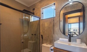 Ein Badezimmer mit Duschkabine, Toilette, Waschbecken und Spiegel sowie einem Fenster.
