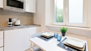 Eine moderne Küche mit weißen Schränken, einer eingebauten Mikrowelle, einer Kaffeemaschine und einem Fenster mit Blick auf Grünflächen.