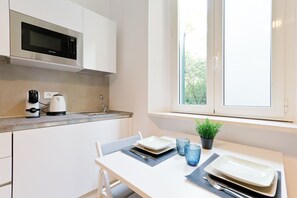 Eine moderne Küche mit weißen Schränken, einer eingebauten Mikrowelle, einer Kaffeemaschine und einem Fenster mit Blick auf Grünflächen.