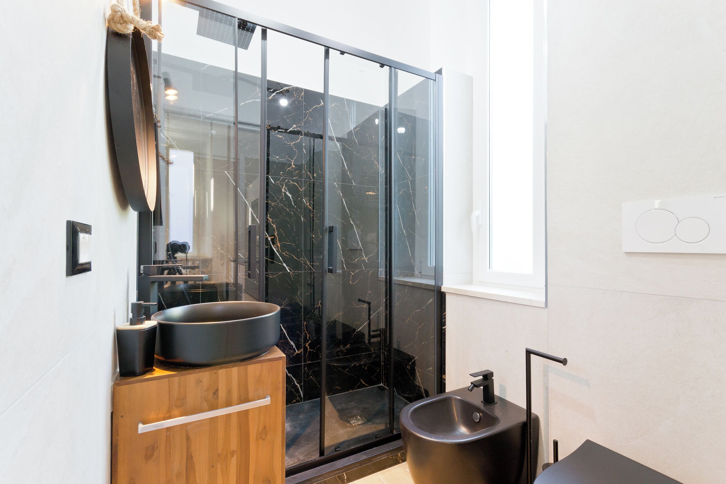 A modern bathroom with a glass shower enclosure, a wooden vanity, a black sink, and a mirror.