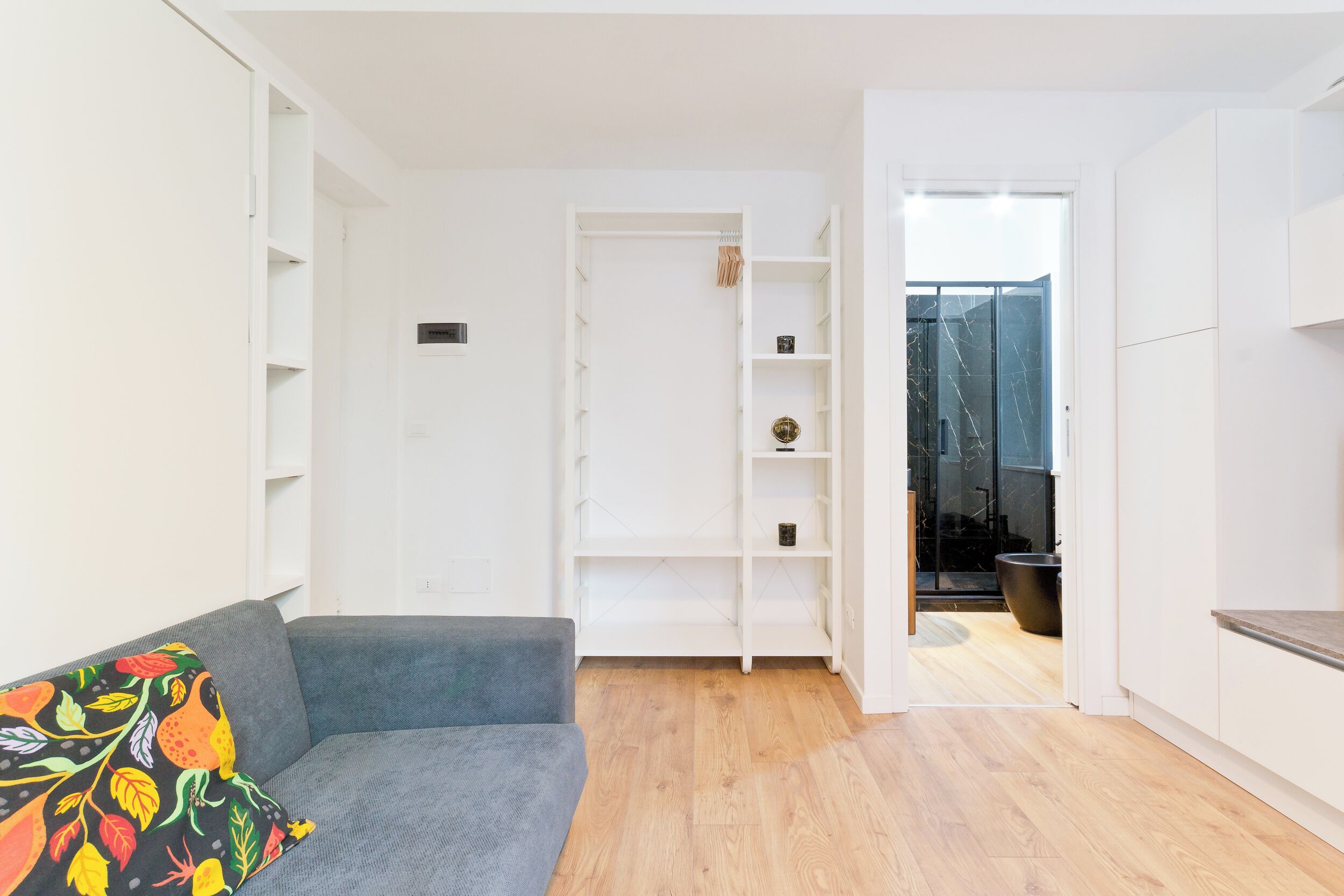 A modern living room with a grey sofa, white shelving units, and a wooden floor.