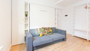 Ein modernes Wohnzimmer mit einem grauen Sofa, einem farbenfrohen Kissen und einem weißen Kleiderschrank mit Regalen.