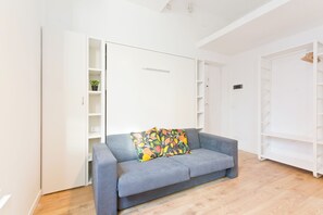 Ein modernes Wohnzimmer mit einem grauen Sofa, einem farbenfrohen Kissen und einem weißen Kleiderschrank mit Regalen.