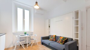 Ein zeitgemäßer Wohnraum mit Essbereich, einer Couch mit bunten Kissen und einem Fenster mit Jalousien.