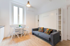 Ein zeitgemäßer Wohnraum mit Essbereich, einer Couch mit bunten Kissen und einem Fenster mit Jalousien.