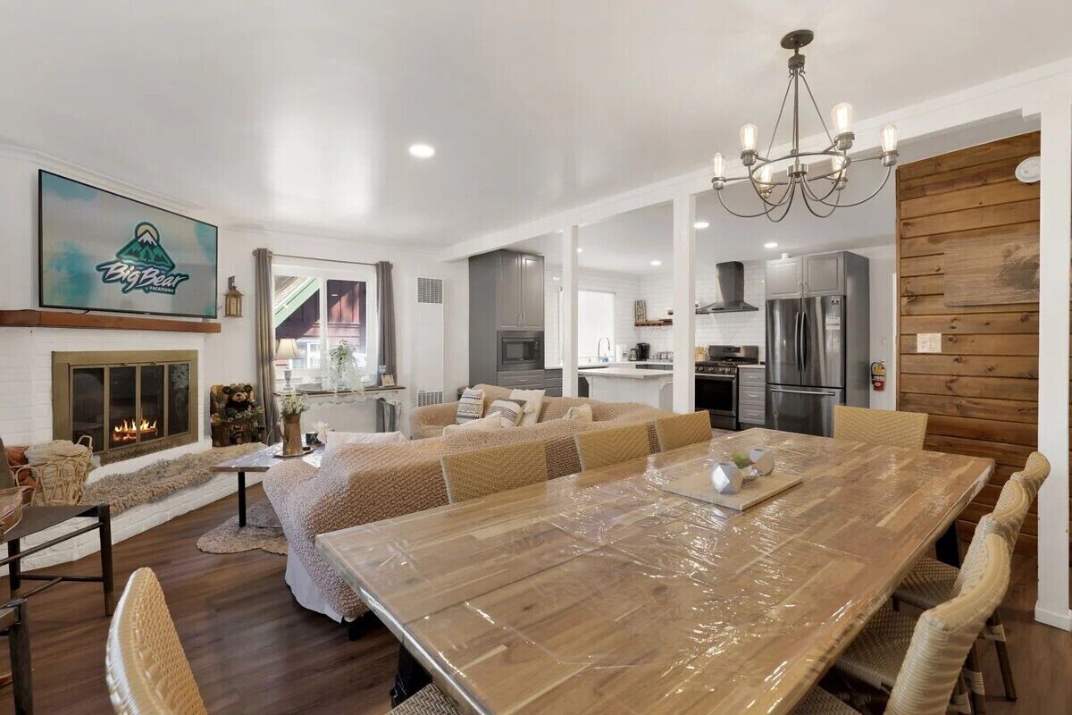 A spacious living area with a large wooden dining table, a fireplace, and a kitchen in the background.