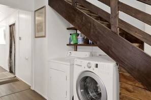 Un espace buanderie comprenant un lave-linge, une étagère avec des produits de nettoyage et un escalier en bois.