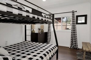 A bunk bed with a checkered bedspread, a desk with a lamp, a window with a view, and a mirror on the wall. - Serenity Peak Big Bear Lake, Family & Groups Mountain Getaway (Big Bear Lake)