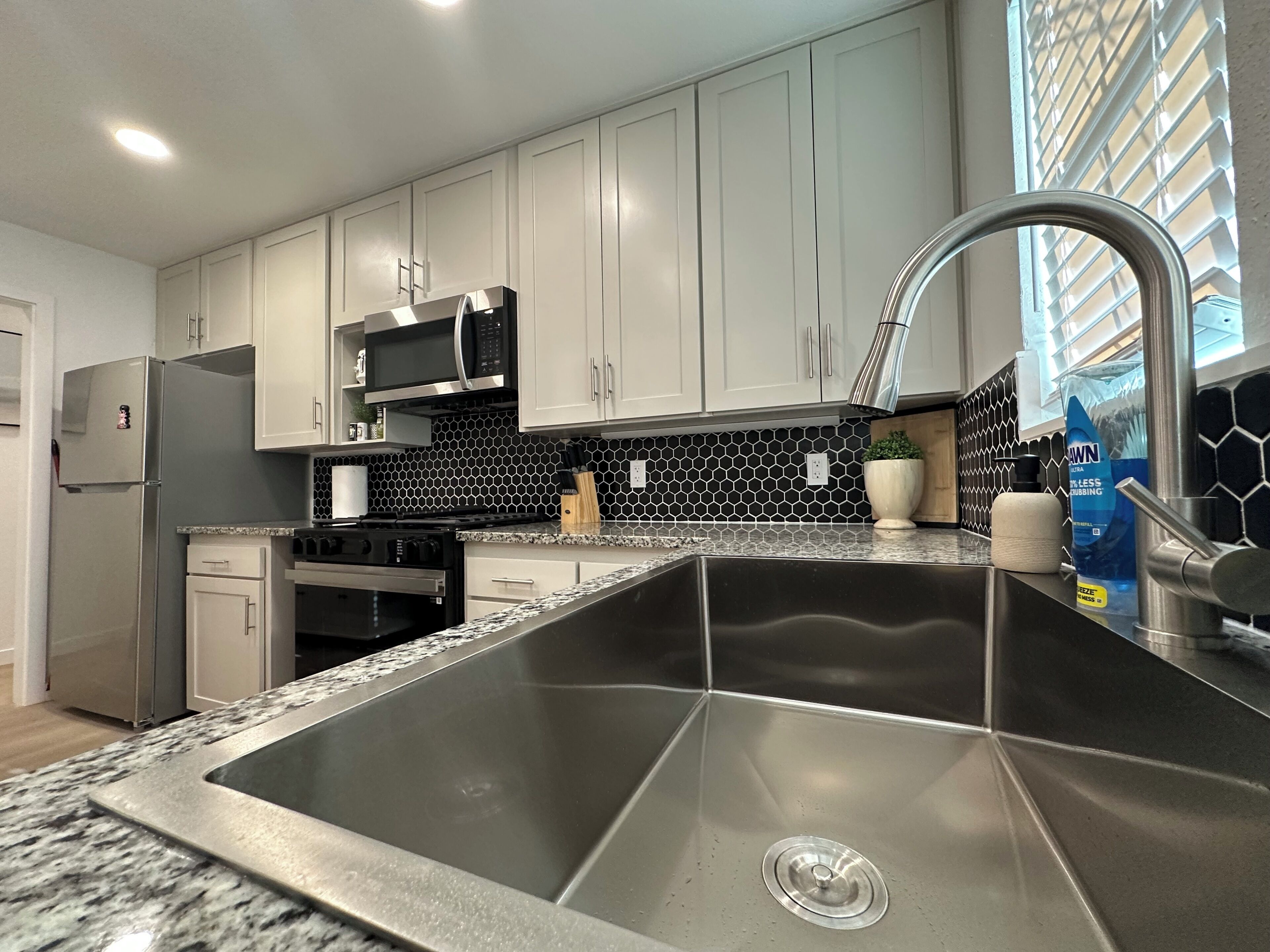A kitchen with white cabinets, a stainless steel sink, a microwave, and a stove.