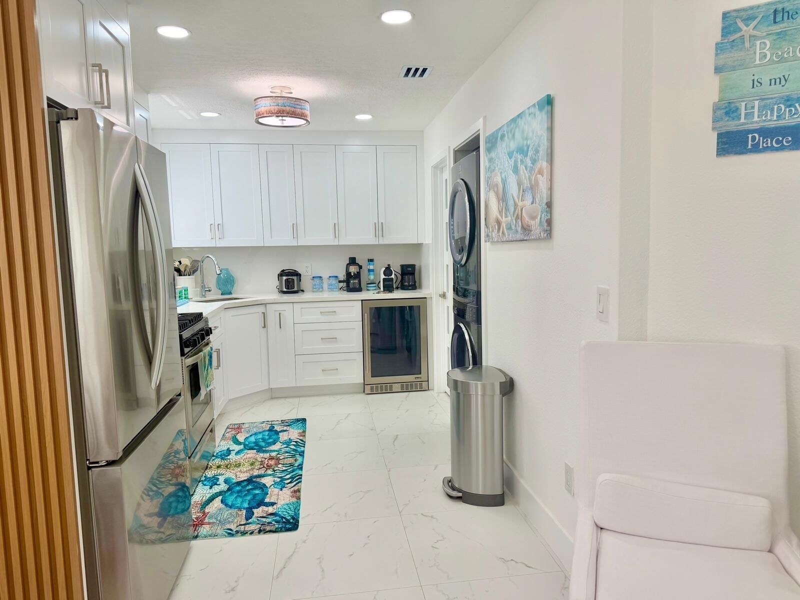 A compact kitchen with white cabinets, a stainless steel refrigerator, a coffee maker, and a trash can.