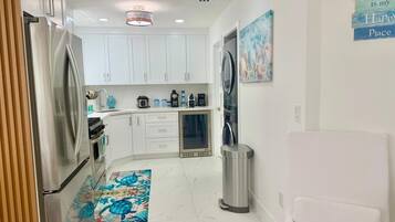 A compact kitchen with white cabinets, a stainless steel refrigerator, a coffee maker, and a trash can.