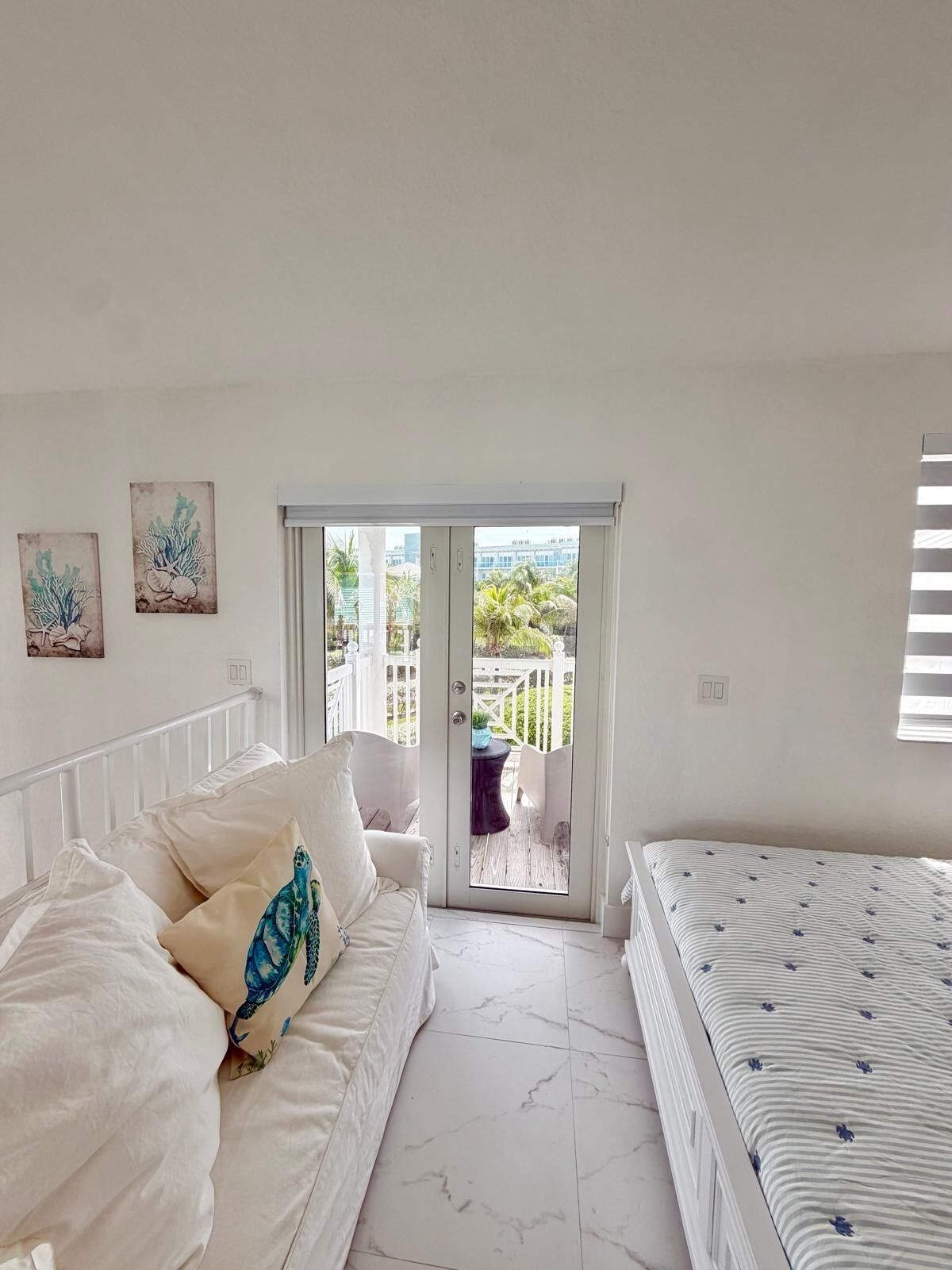 Un dormitorio con cama y sofá blancos, y vista a un balcón con valla blanca.