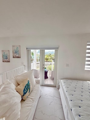 Un dormitorio con cama y sofá blancos, y vista a un balcón con valla blanca.