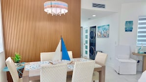Comedor con pared de paneles de madera, una araña y un modelo de velero, con una lavadora al fondo.