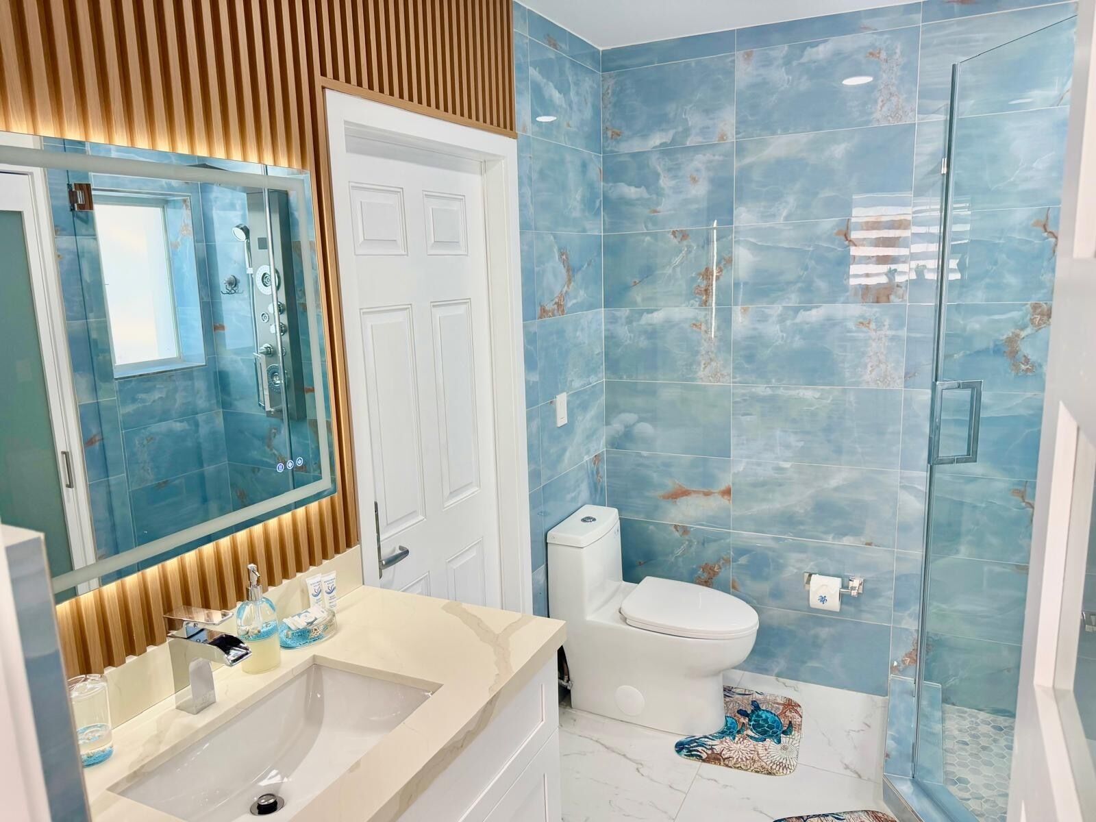 A bathroom with a shower, toilet, and sink, featuring blue tiles and a wooden panel design.