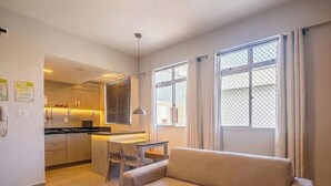 Un espacio habitable compacto con kitchenette, comedor y un amplio ventanal con cortinas.