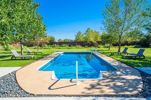 Ein rechteckiger Swimmingpool mit glasklar blauem Wasser, umgeben von einer Betonplattform. Auf beiden Seiten des Pools stehen jeweils zwei Liegestühle, und im Hintergrund ist ein Holzzaun zu sehen.