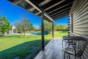 Un patio techado con una mesa y sillas, una piscina y un jardín cubierto de césped.