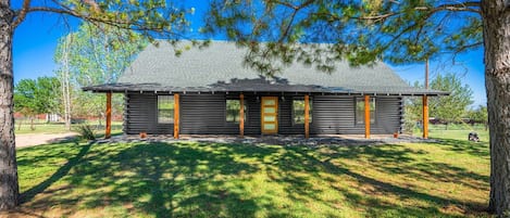 A log cabin with a gabled roof, a front porch with wooden posts, and a fenced yard.