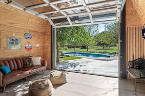 Een modern interieur met een houten plafond, een leren bank, een zwembad buiten en uitzicht op een groen landschap.