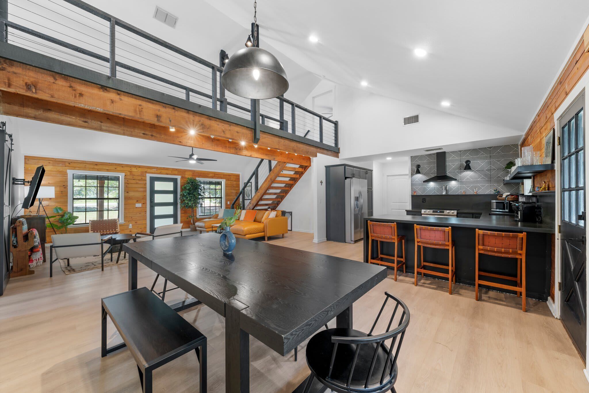A spacious kitchen with a central island, a dining area with a large table, and a staircase leading to an upper level.