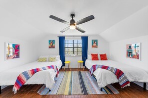 Ein Zimmer mit zwei Betten, einem Deckenventilator, einem fenster mit Vorhängen und Bildern an den Wänden.