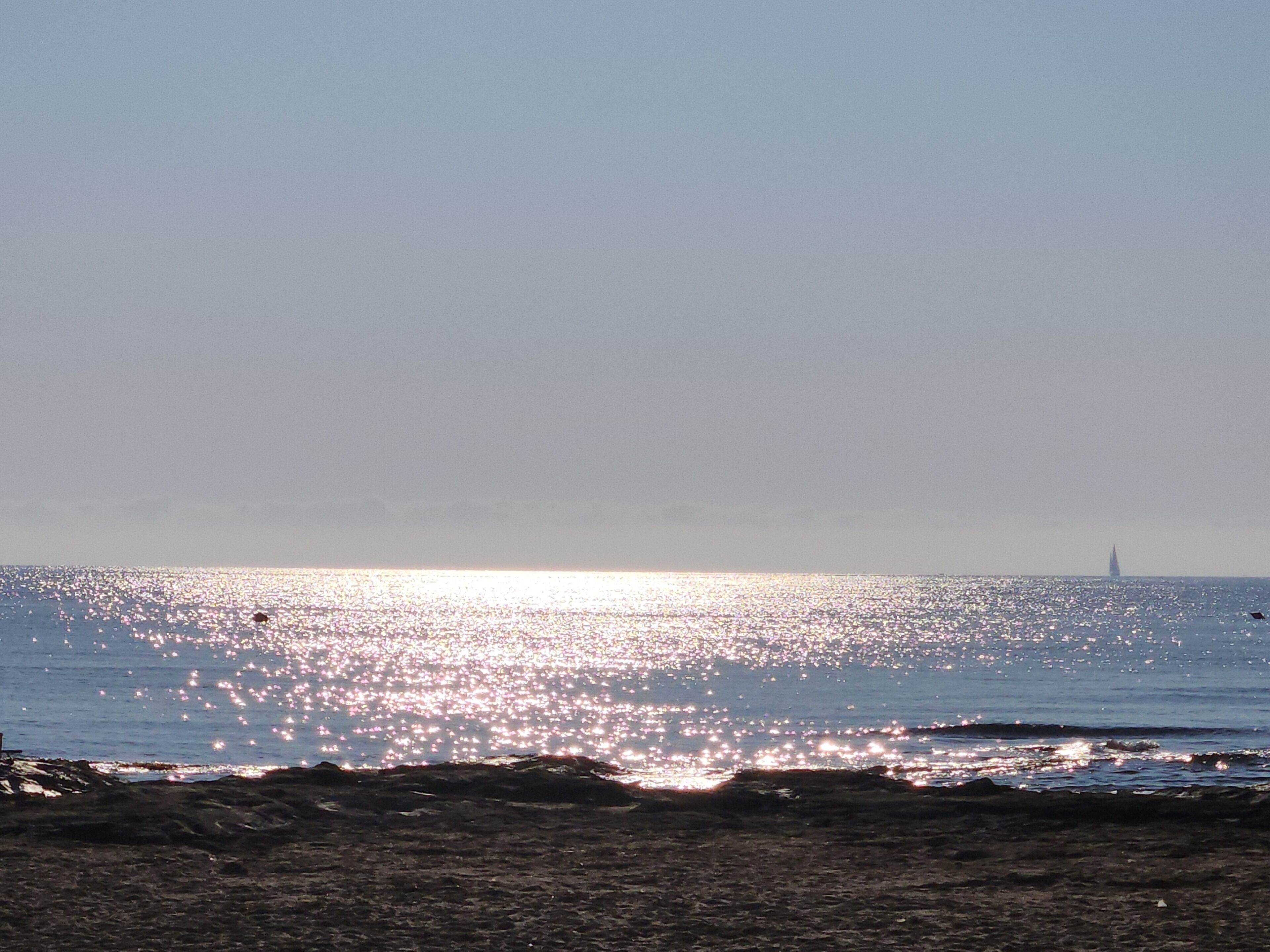 Ein Strand mit blauem Himmel und einem fernen Leuchtturm.