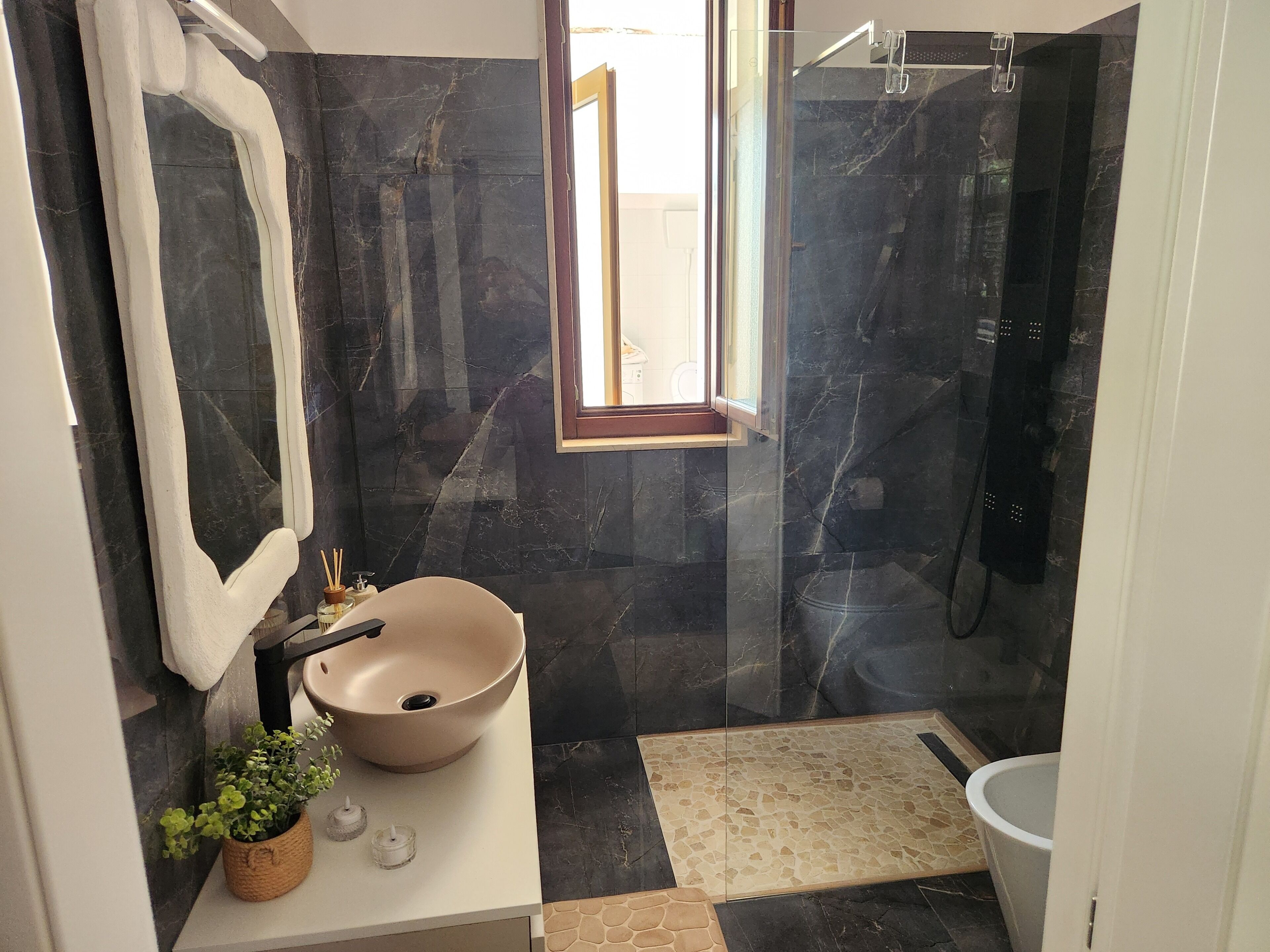 Een badkamer met een beige wastafel, een spiegel, een potplant en een douchehoek.