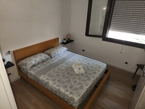 A single bed with a wooden headboard, a bedside table with a lamp, and a window with blinds.