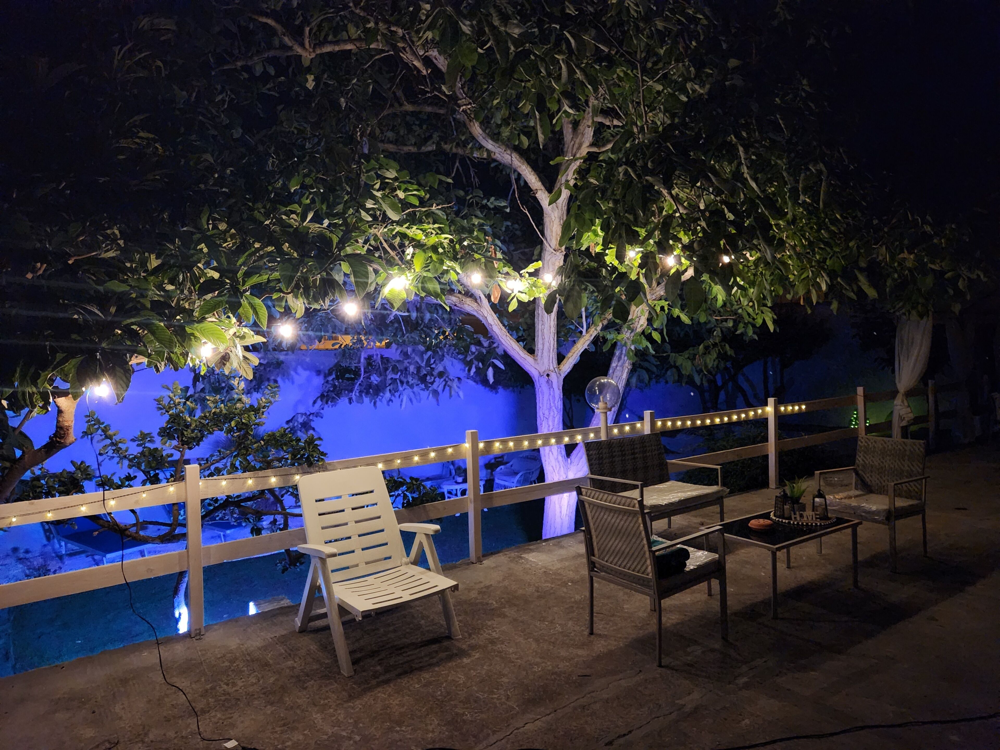 An outdoor seating area with chairs and tables, a wooden fence, and string lights under a tree.