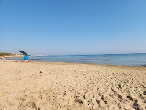 A sandy beach with footprints, a blue umbrella, and a clear sky.