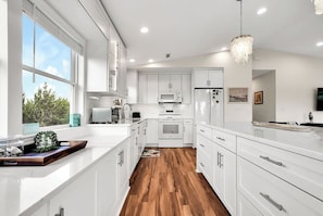 A modern kitchen with white cabinetry, a wooden floor, and a view of the outdoors.