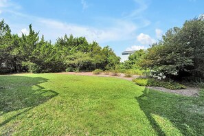 A well-maintained grassy area with trees and shrubs, a clear sky, and a building in the background. - SURF AND SOUND- Enjoyable 3-bedroom house with AC in Topsail Beach (Topsail Beach)