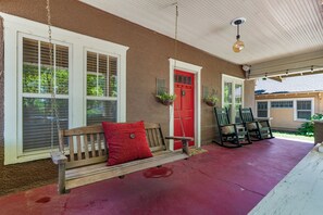 A porch with a wooden bench, a red door, and a hanging light fixture. - Charming 3-bedroom house in Tulsa with cool AC and comfort (Tulsa)