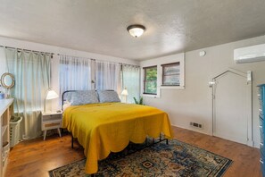 A bedroom with a bed, bedside table, lamp, curtains, window, air conditioning unit, and a patterned rug. - Charming 3-bedroom house in Tulsa with cool AC and comfort (Tulsa)