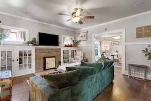 A living room with a green sofa, a flat-screen TV, a fireplace, and a ceiling fan. - Charming 3-bedroom house in Tulsa with cool AC and comfort (Tulsa)
