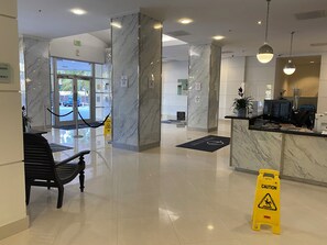A clean, modern lobby with marble columns, a reception desk, and a bench. - Sunny Isles, beach life! Parking included (Sunny Isles Beach)