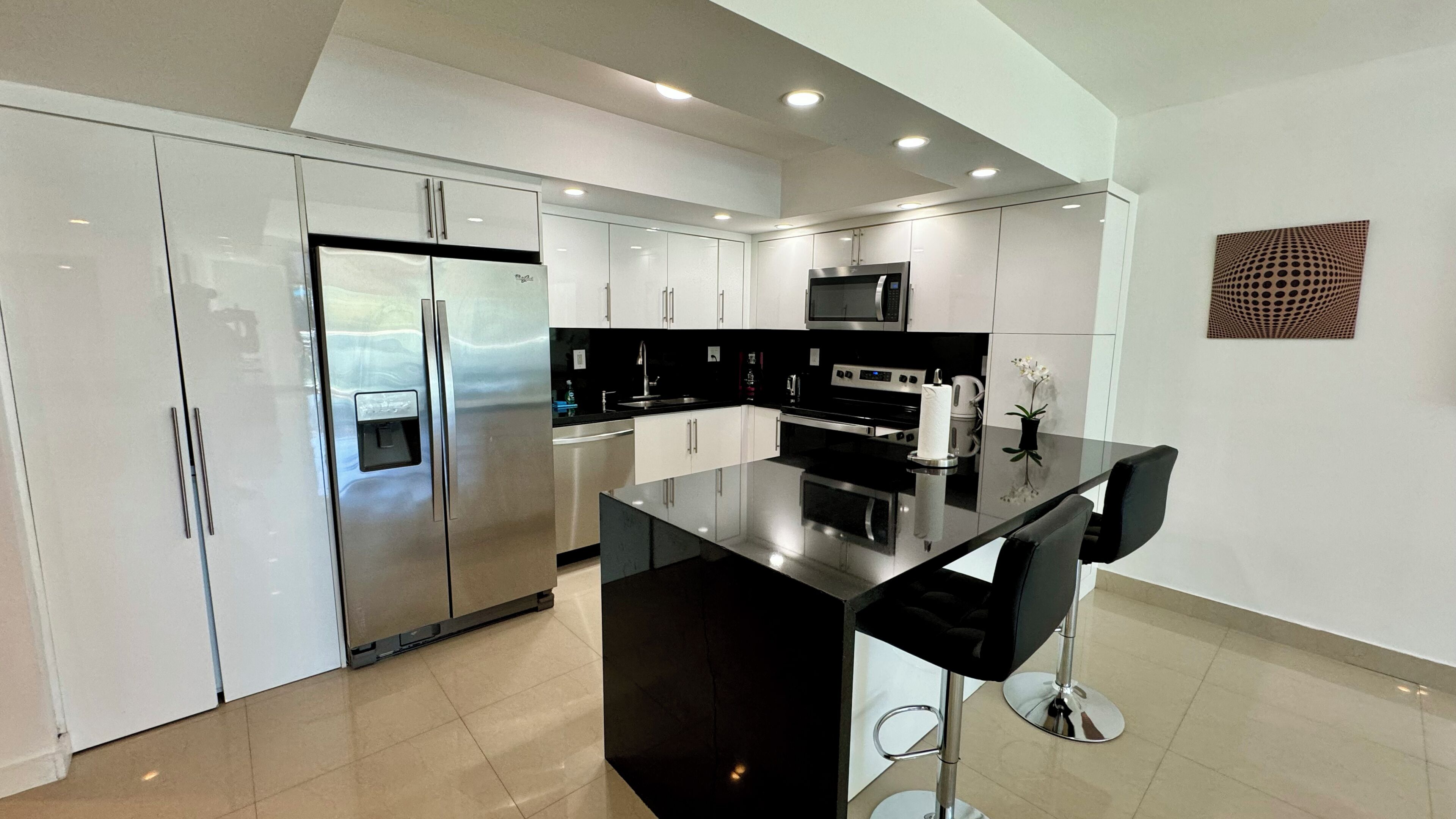 A modern kitchen with stainless steel appliances, a black countertop, and a white tiled floor.