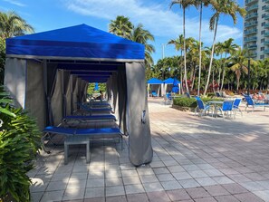 A covered outdoor seating area with blue chairs and tables, surrounded by palm trees and a tall building in the background. - Sunny Isles, beach life! Parking included (Sunny Isles Beach)
