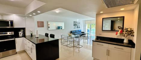 A modern kitchen with a central island, dining area, and a large window.