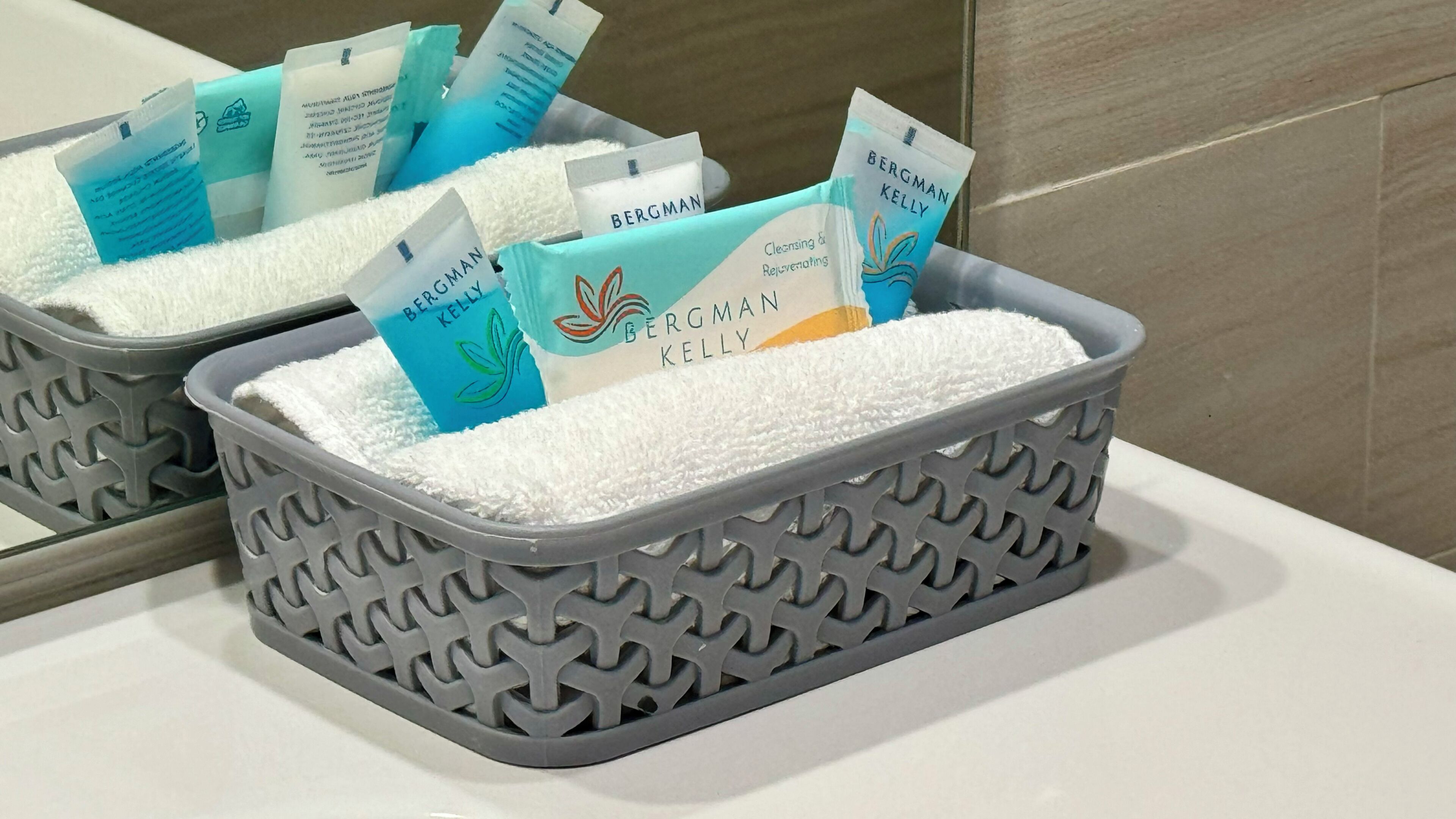 Un baño con espejo, lavamanos y una bandeja gris estampada con artículos de aseo.