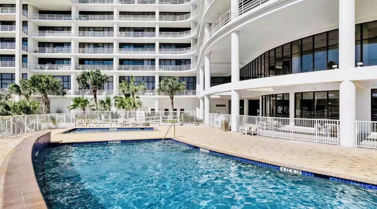 A modern hotel with a multi-level pool area, outdoor seating, and a white facade.