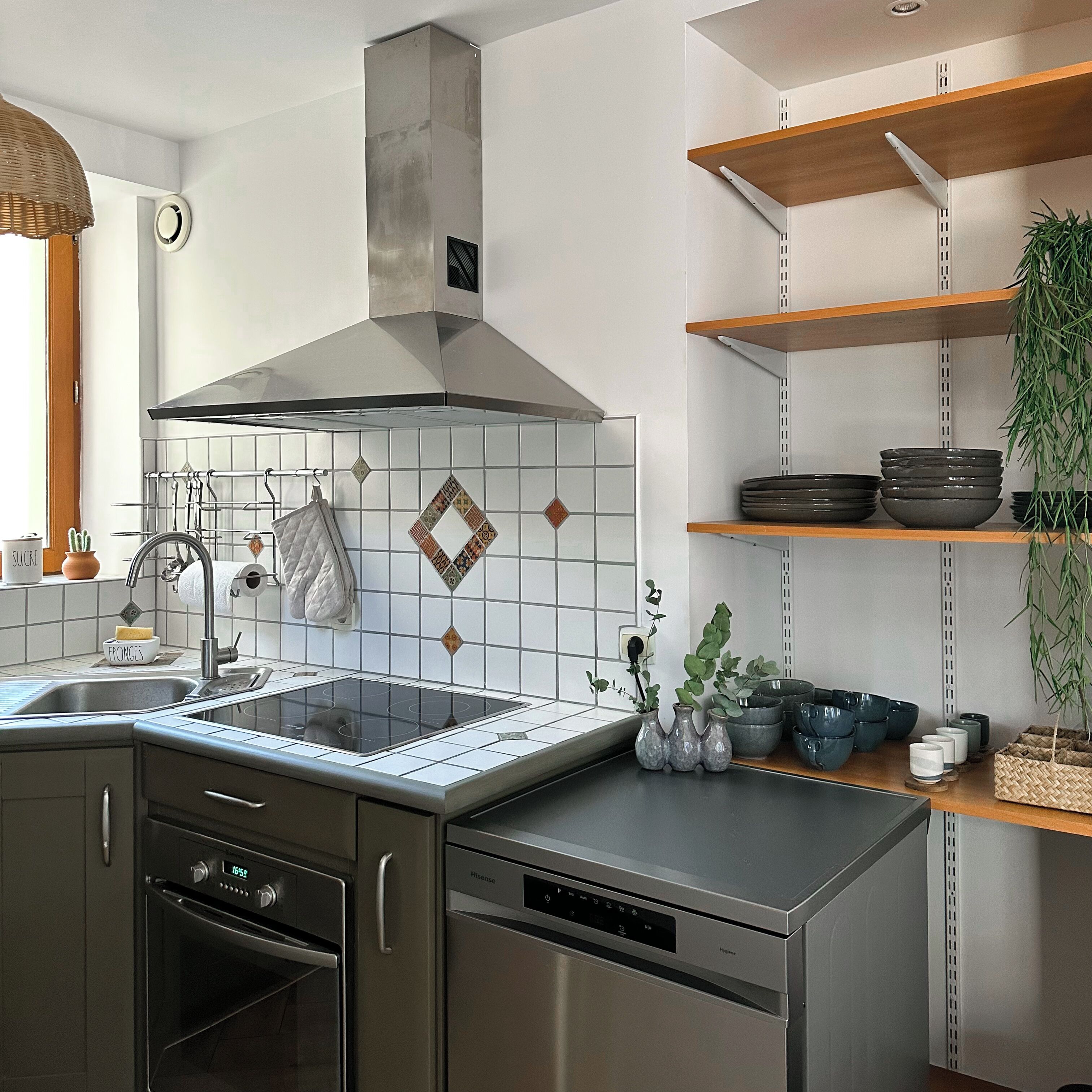 A modern kitchen with a stainless steel range hood, a built-in dishwasher, and a window above the sink.